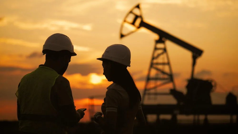 Silhouette of a oilfield workers meeting at a crude oil pump unit at sunset