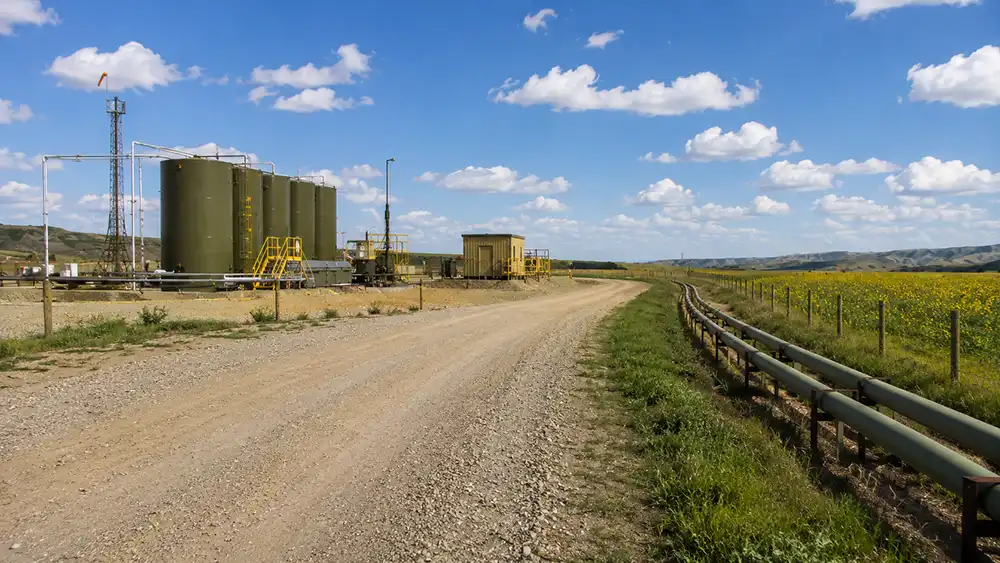 Oil storage tanks and surface pipelines along a gravel lease road on agricultural property